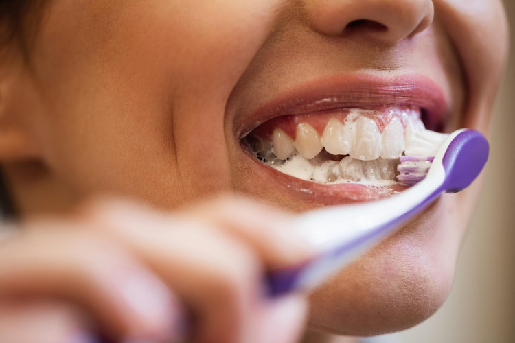 a woman is brushing her teeth with a safe toothpaste.