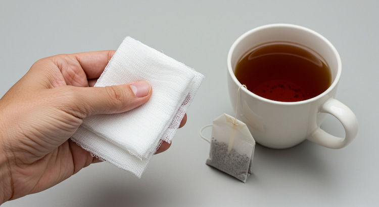 a hand holding a gauze and a tea bag next to it for wisdom tooth extraction aftercare.